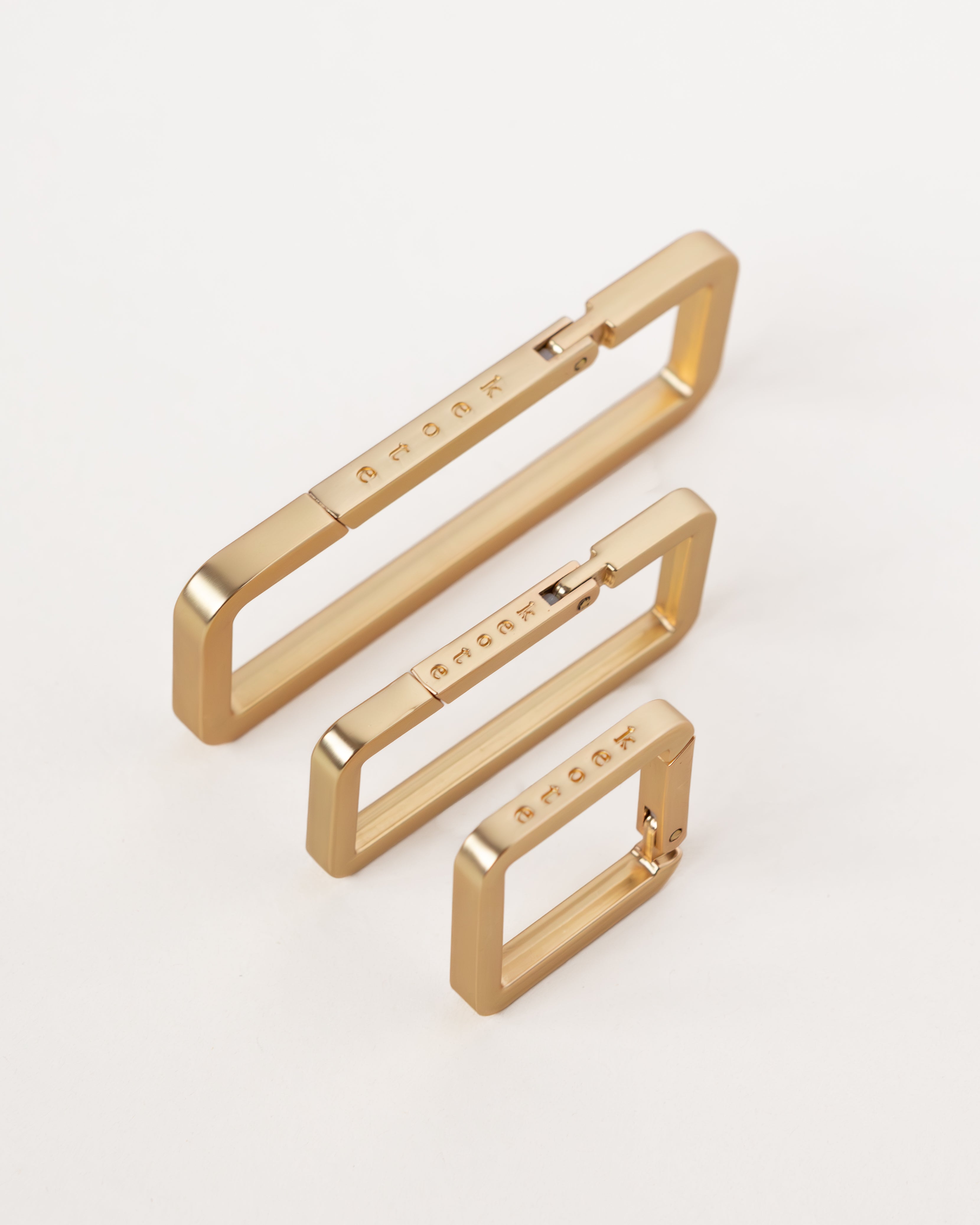 Three gold-colored metal key rings of different sizes designed to wrap around purse straps, displayed on a white background.